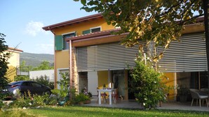 A two-story house with a stone chimney, a car parked in the driveway, and a patio area with a table and chairs. - B&B Mimosa e Lillà (Fumane)