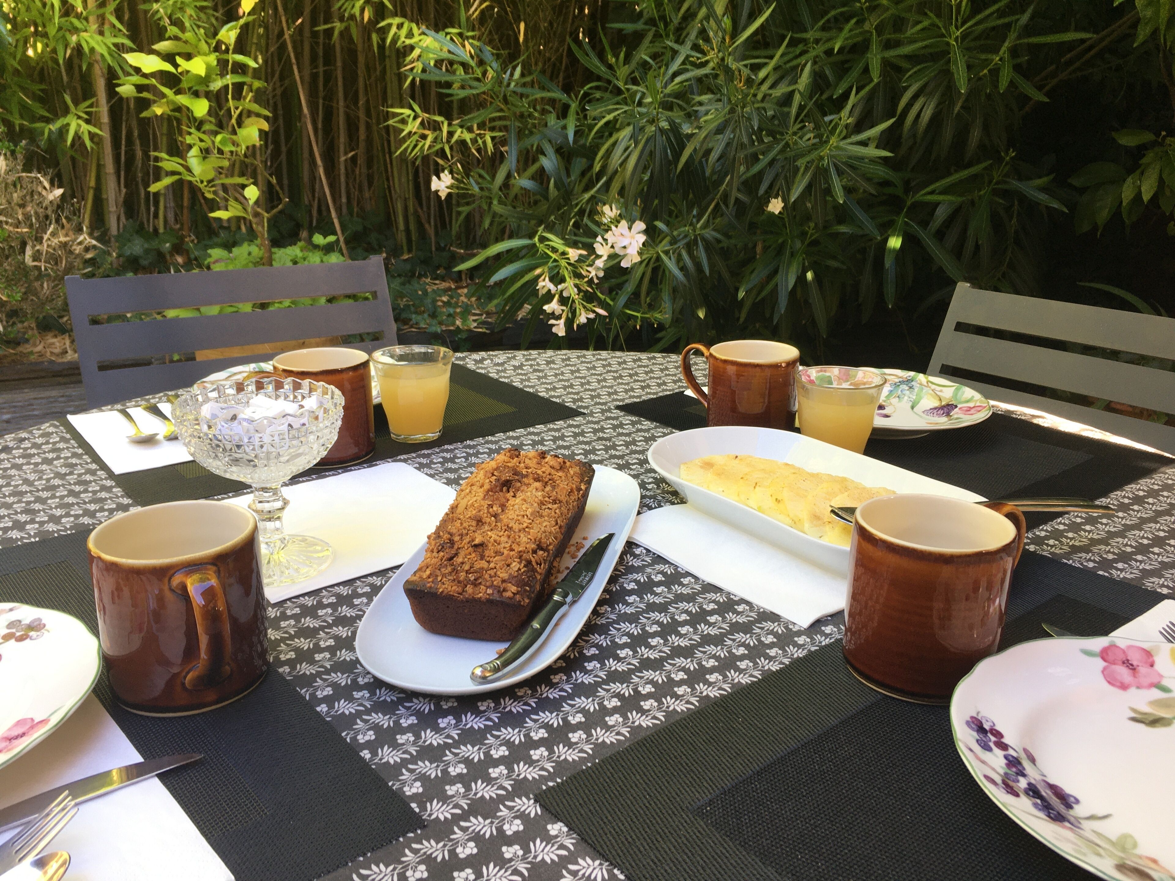 Une table dressée à l’extérieur, avec une variété de plats, notamment une miche de pain, une assiette de nourriture, ainsi que plusieurs tasses et bols.