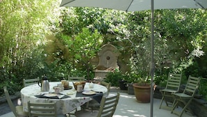 An outdoor patio with a round table set for dining, surrounded by chairs, and a large umbrella providing shade. - Blue Lodge in Bordeaux (Bordeaux)