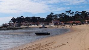 A beach with a boat on the shore, a sandy beach, and houses in the background. - Blue Lodge in Bordeaux (Bordeaux)