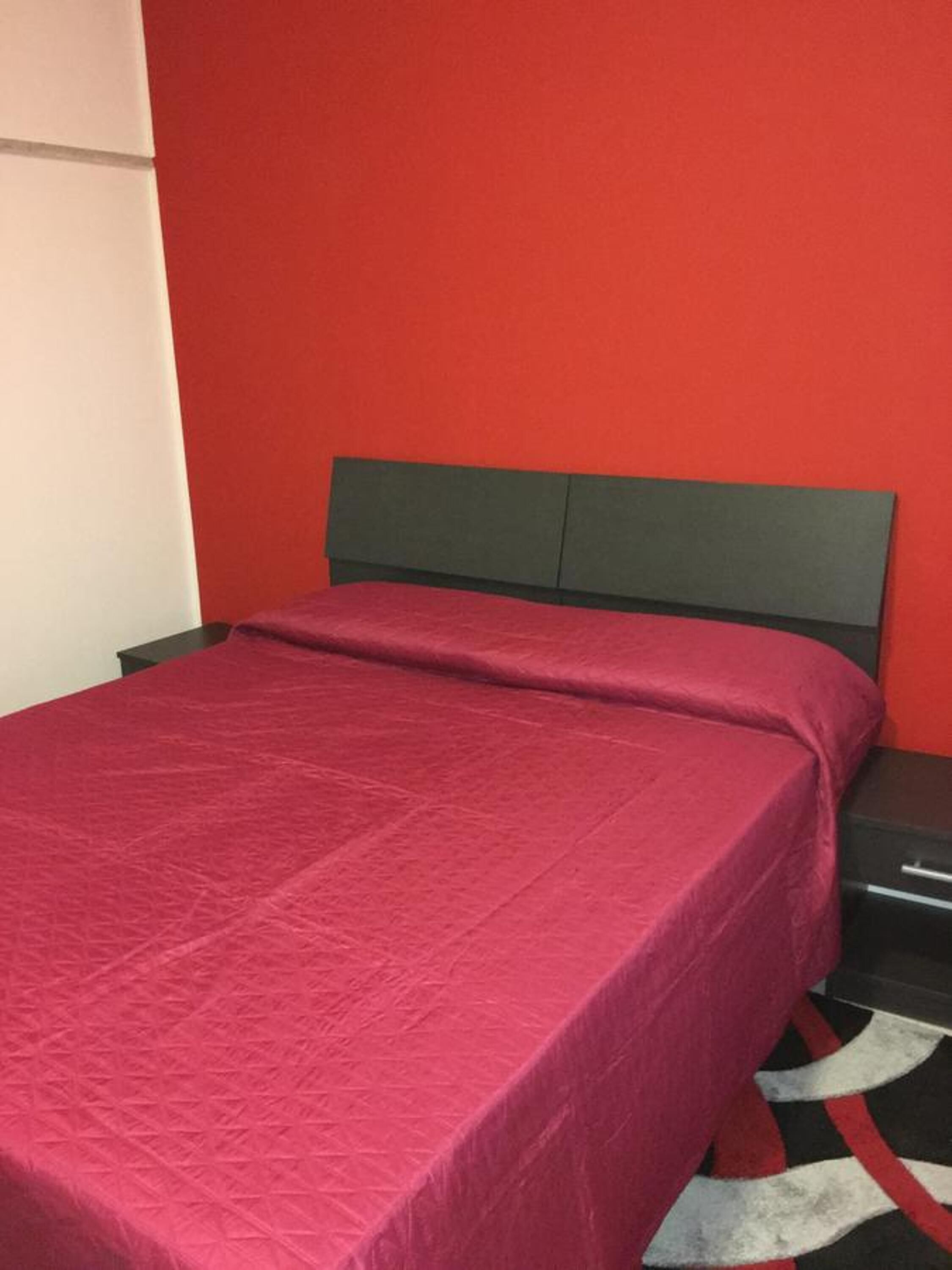 Una habitación con una cama, una mesita de noche y una pared roja.