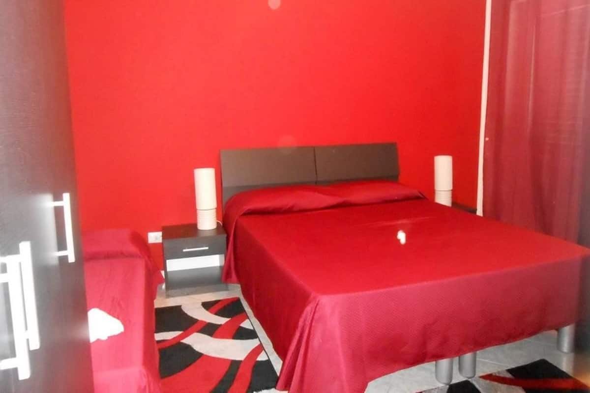 Quarto com cama, mesa de cabeceira, abajur e parede vermelha.