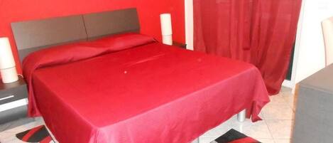 Una cama con una colcha roja, un cabecero gris y una alfombra estampada.