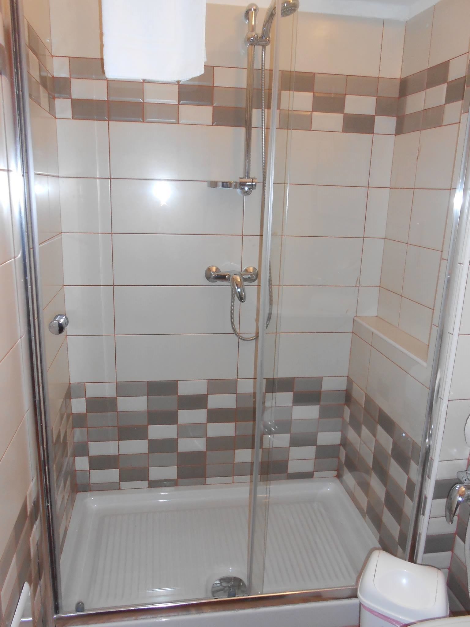 Una ducha con puerta de vidrio, inodoro blanco y paredes con zanjas de diseño ajedrezado.
