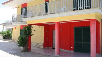 A two-story building with a balcony, a palm tree, and a red and yellow facade.