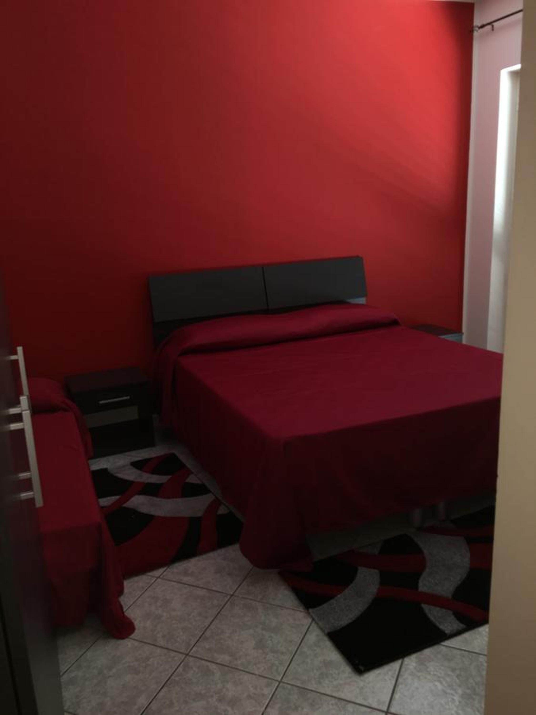 A bedroom with a red bedspread, a black headboard, a nightstand, and a red chair.