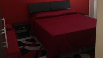 Una camera da letto con una coperta rossa, un poggiatesta nero, un comodino e una sedia rossa.