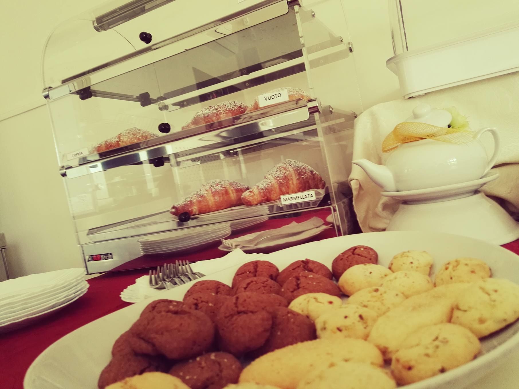 Una vitrina de panadería con pasteles y galletas, una cafetera y un plato de galletas.