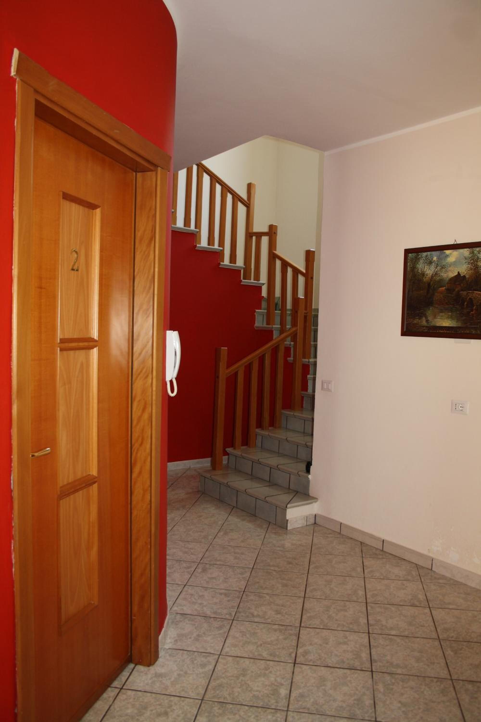 Ein Flur mit einer Holztür mit der Aufschrift '2', einer Holztreppe mit Geländern und einem Bild an der Wand.