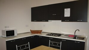 A compact kitchen with black cabinets, a white countertop, a microwave, a gas stove, and a sink. - B&B Paradiso (Falerna)