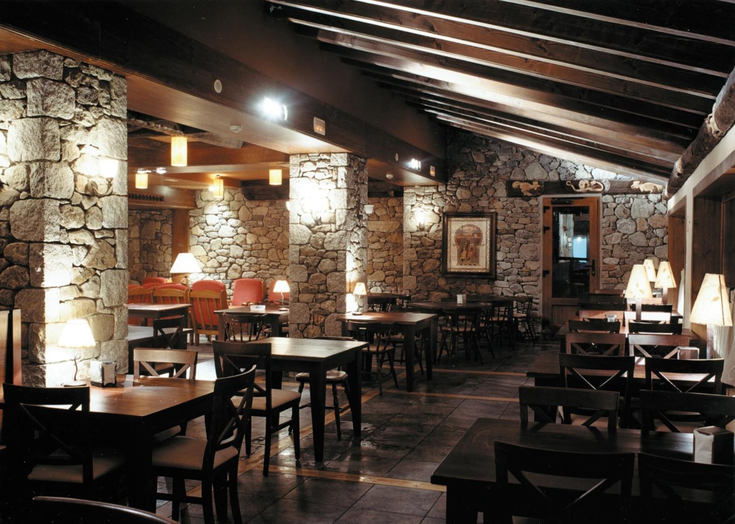 A restaurant with stone walls, wooden tables, and chairs.