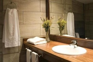 A bathroom with a wooden vanity, a white sink, and a mirror. There are towels hanging on the wall and a vase with flowers on the vanity. - Hotel Hospital de Benasque (Benasque)