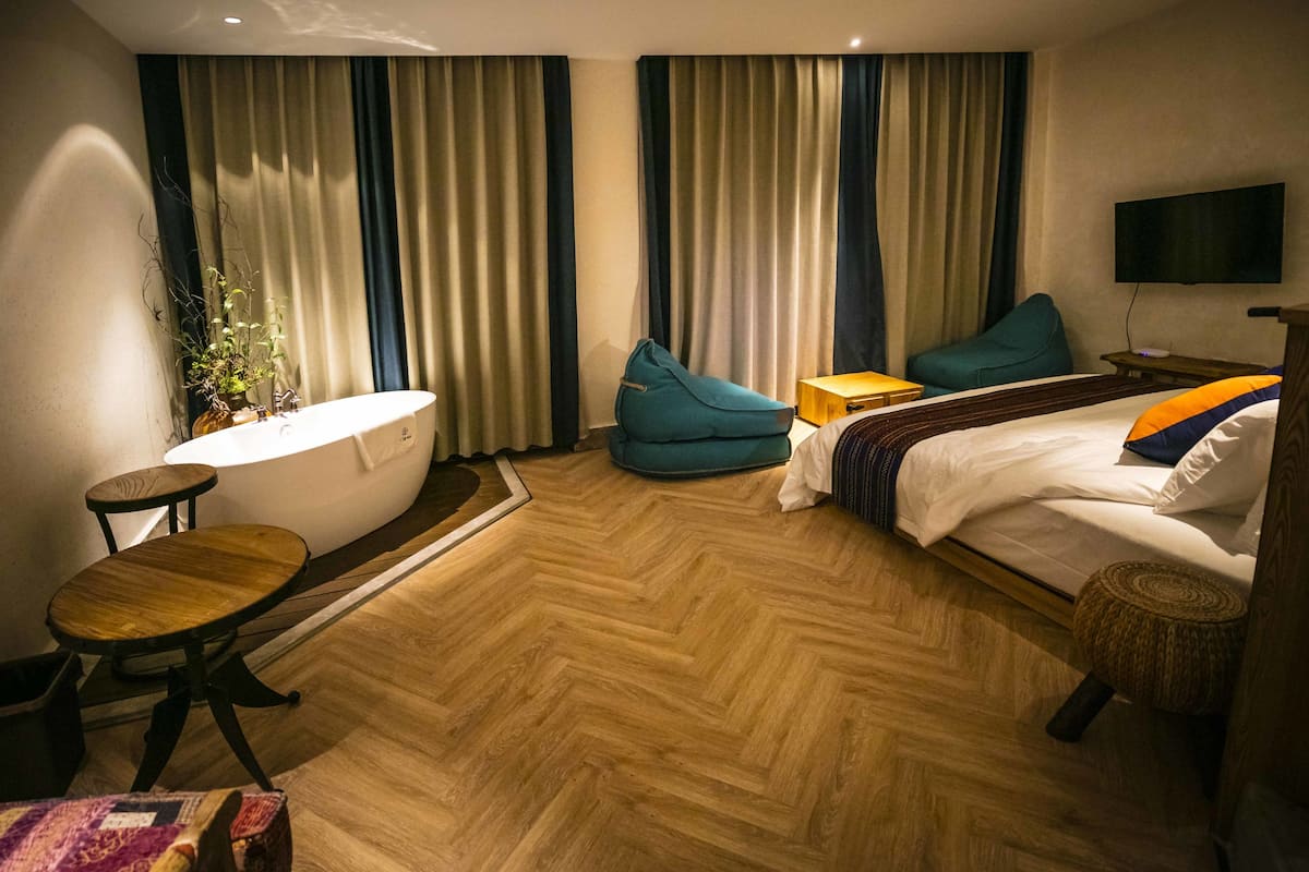 A hotel room with a bathtub, a bed with pillows, a small table, and a television on the wall.