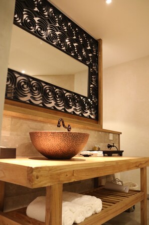 A wooden vanity with a copper vessel sink, a mirror with a decorative frame, and a towel rack.