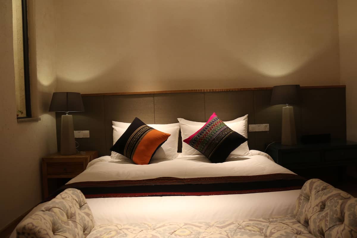 A neatly made bed with white linens and decorative pillows, a wooden headboard, and bedside lamps.