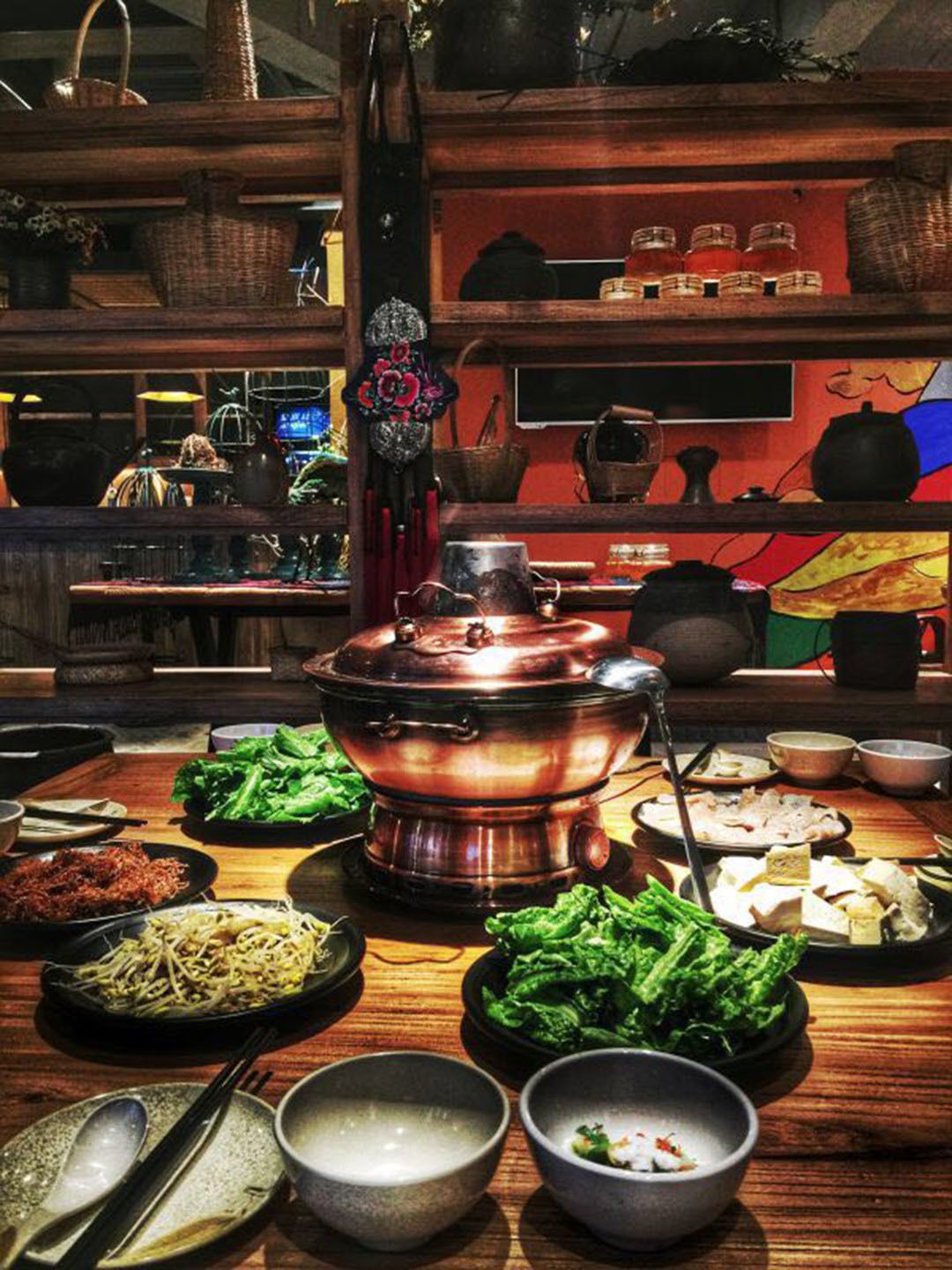 Un restaurante asiático tradicional con un recipiente central para fondue, varios platos y una decoración de madera.