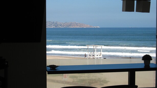 Vista del océano desde una ventana con vista a una playa y una torre de salvavidas.
