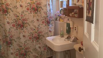 Un baño con cortina de ducha estampada con motivos florales, un lavabo blanco, un inodoro de madera y un espejo sobre el lavabo.