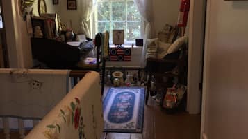 A cozy room with a wooden floor, a window with sheer curtains, and various framed pictures on the walls.