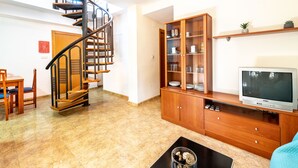 A living room with a spiral staircase, wooden furniture, a television, and a cabinet with glass doors. - Residencial Marcomar Casa Azahar (Alcala de Xivert)