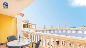 A balcony with a round table and chairs, a bottle of wine, and a view of buildings in the background. - Residencial Marcomar Casa Azahar (Alcala de Xivert)