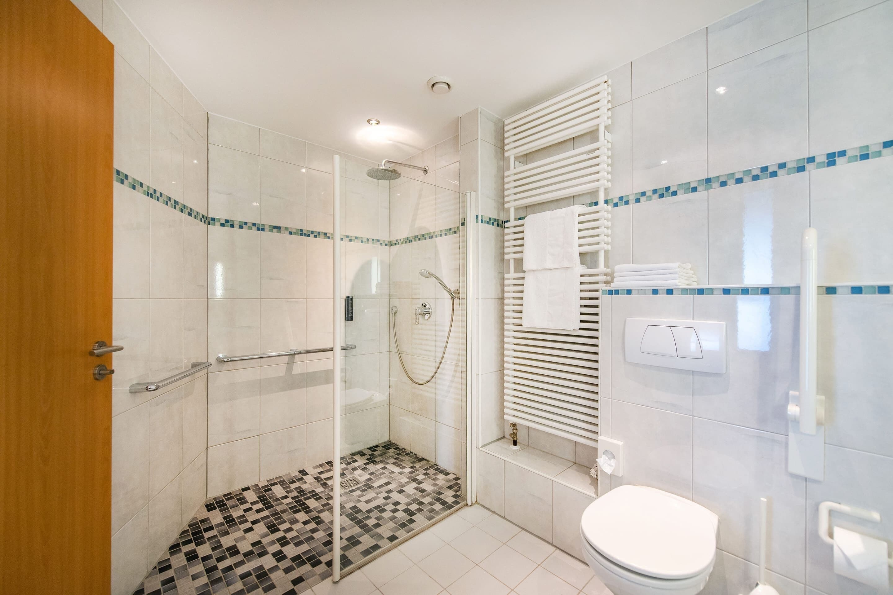 Un baño moderno con ducha de vidrio, un inodoro blanco y piso de baldosas con diseño de tablero de ajedrez.