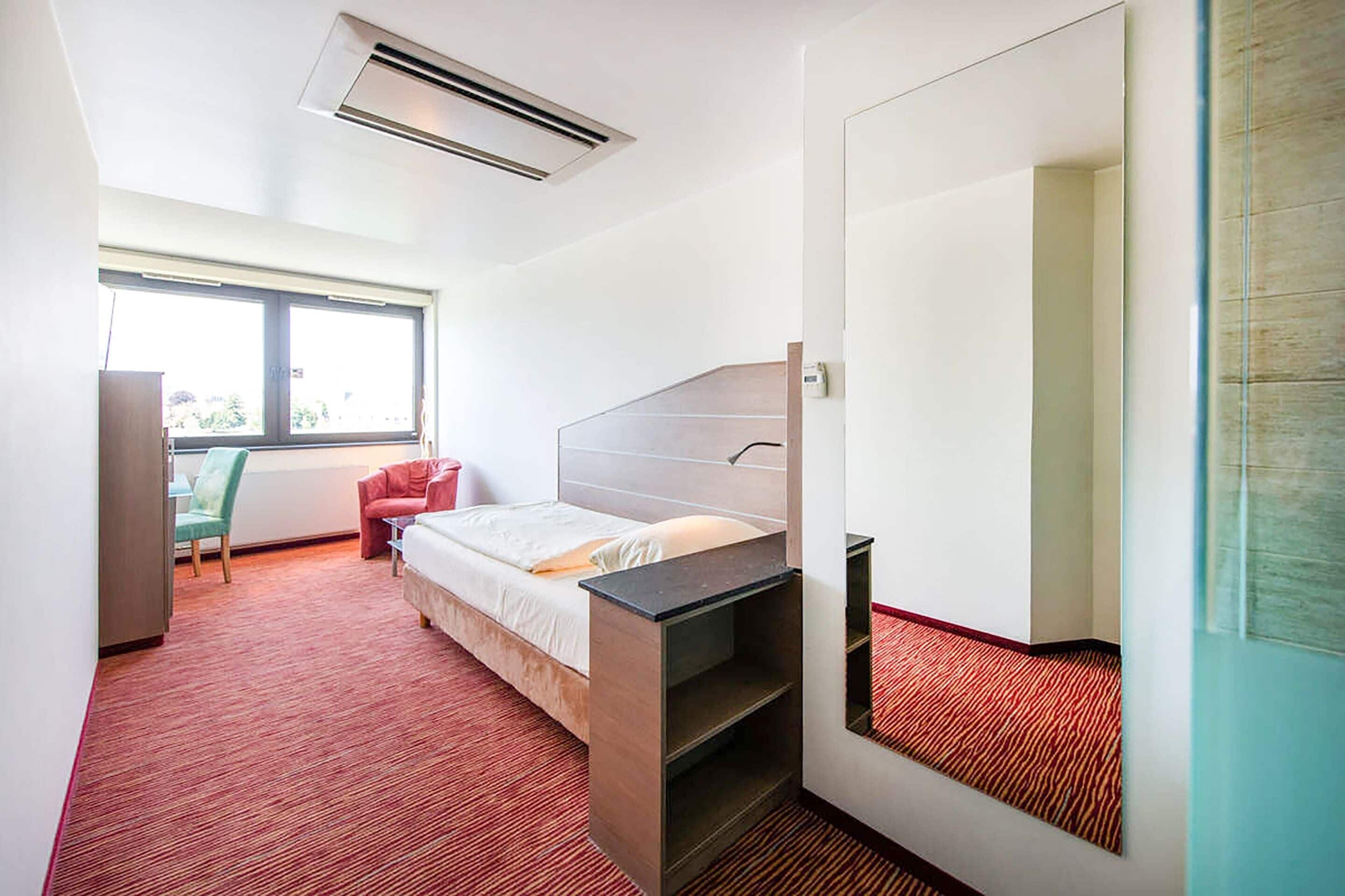 A hotel room with a bed, a desk, a chair, and a large window.