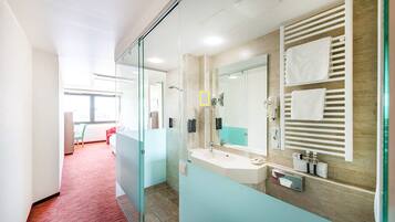 Un baño de hotel moderno con mampara de vidrio, un espejo grande, un perchero y un lavamanos.