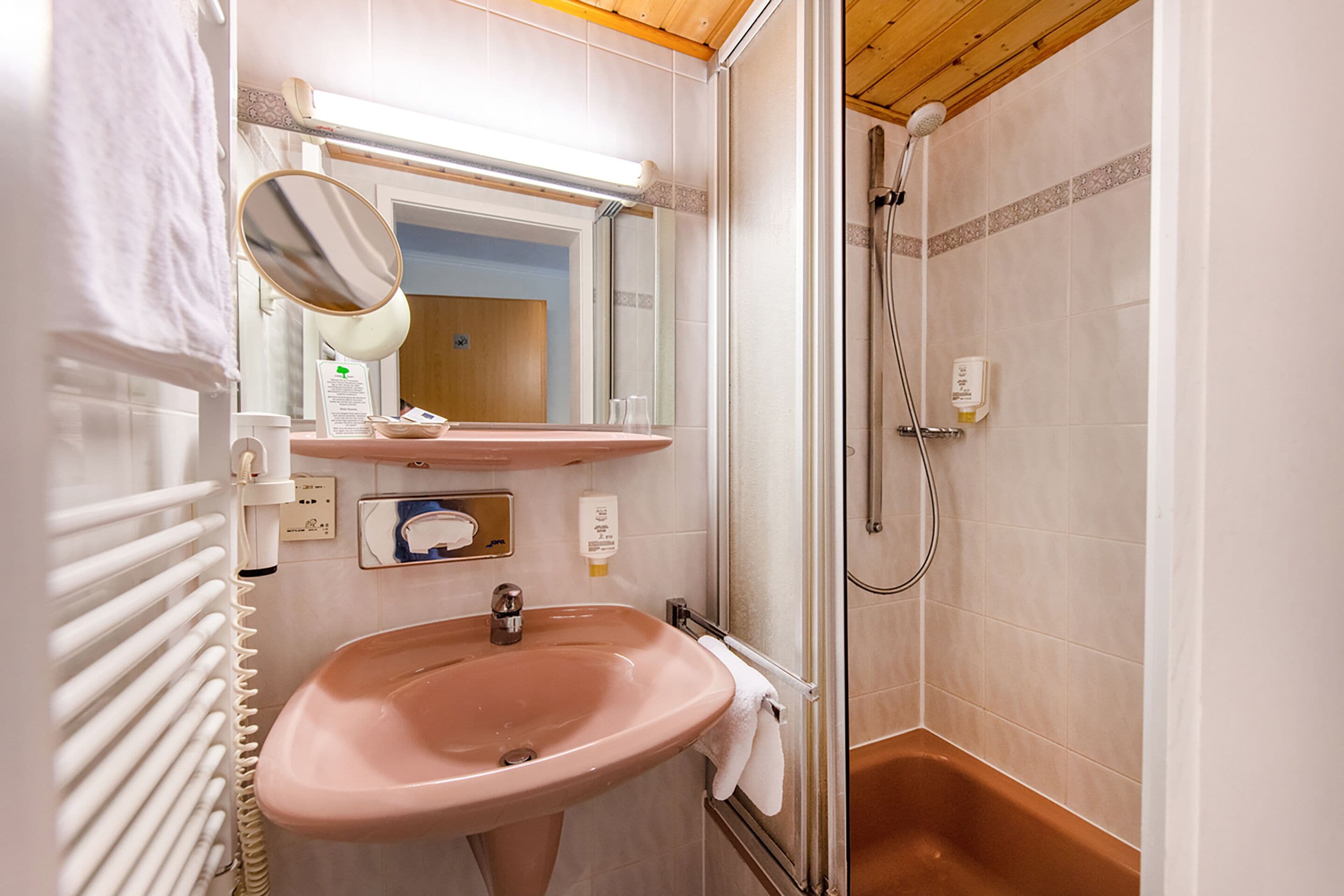 Un baño con lavamanos rosa, un espejo, ducha y toallero.