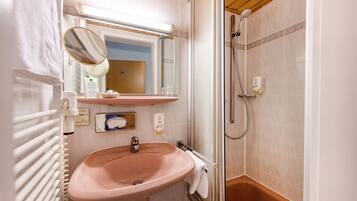 Un baño con lavamanos rosa, un espejo, ducha y toallero.