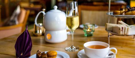 Una mesa con un juego de té, una copa de vino blanco, una taza de té, un plato con macarons y un pastelillo con sándwiches.