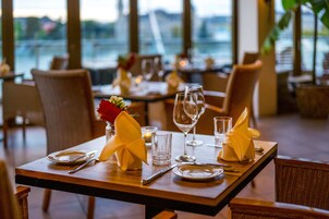 Una mesa de comedor dispuesta con platos, cubiertos, vasos y servilletas, con vistas al exterior a través de amplios ventanales.