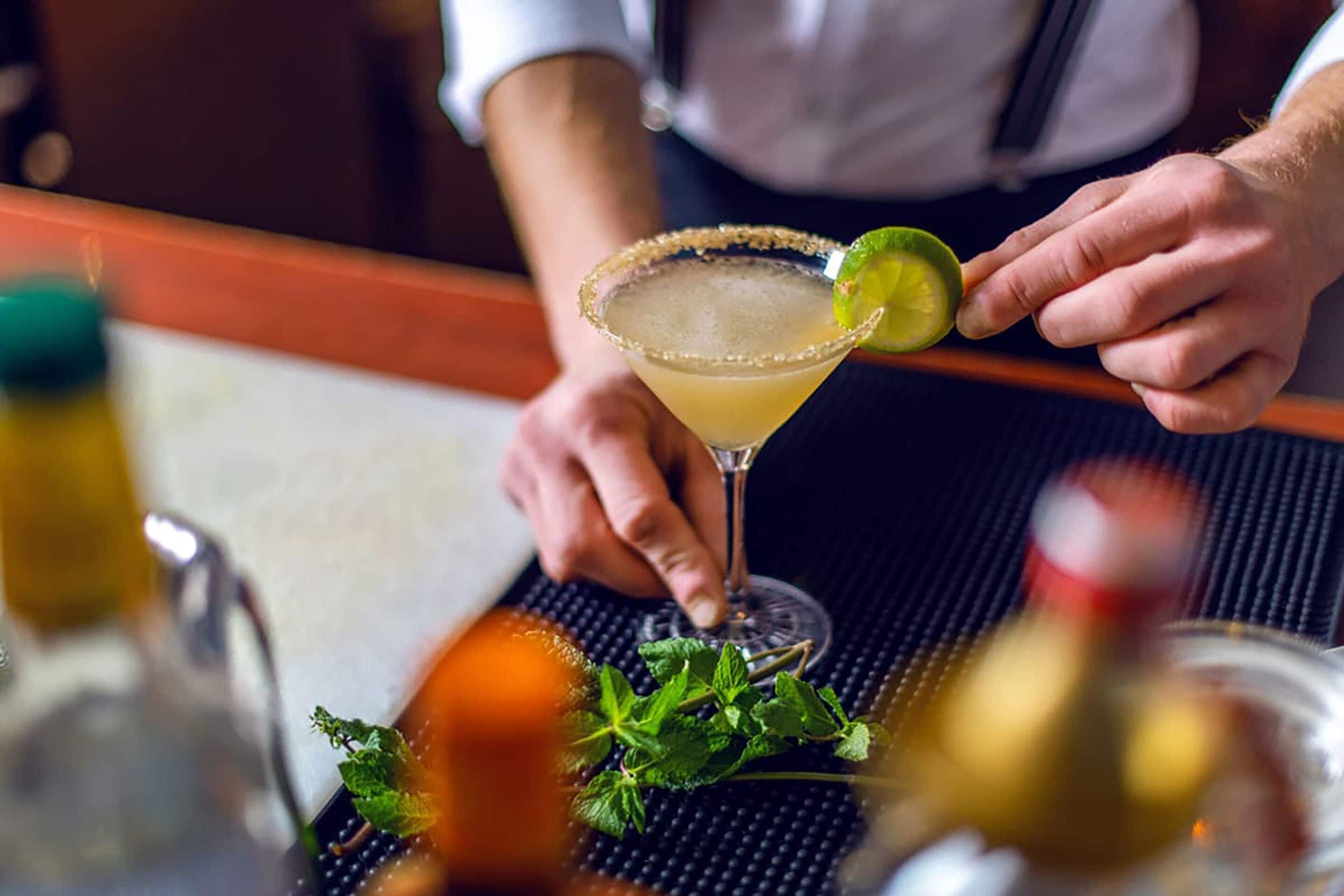 A person preparing a cocktail with a lime garnish on a bar counter.
