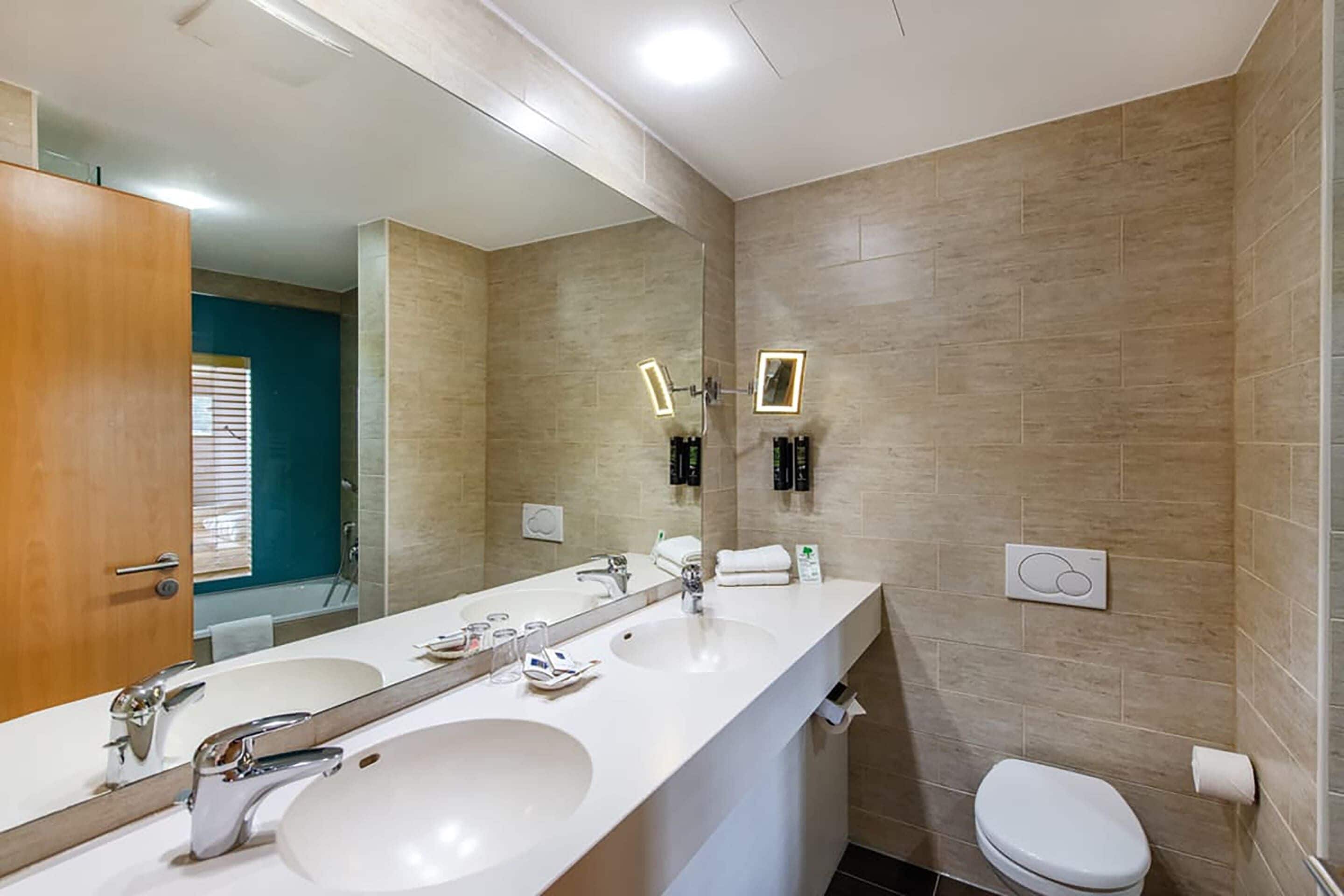 A modern bathroom with two sinks, a large mirror, and a toilet.