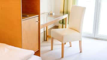 A hotel room with a wooden desk, a white chair, and a bed.