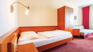 Habitación de hotel con cama de madera, mesita de noche, alfombra roja y lámpara de pared.
