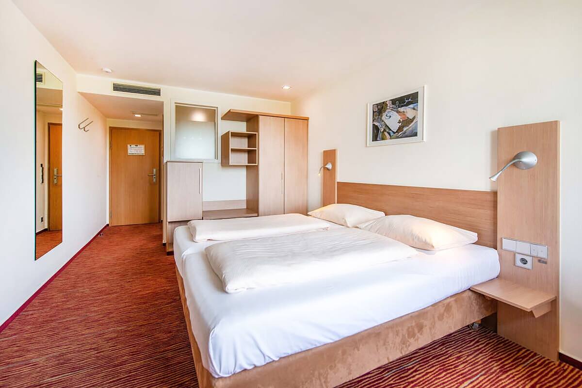 Habitación de hotel con dos camas, cabecero de madera, un escritorio pequeño, un espejo y un cuadro en la pared.