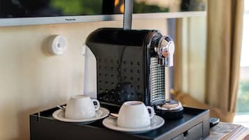 A coffee machine with two white cups on a tray, a power outlet, and a window with a view.