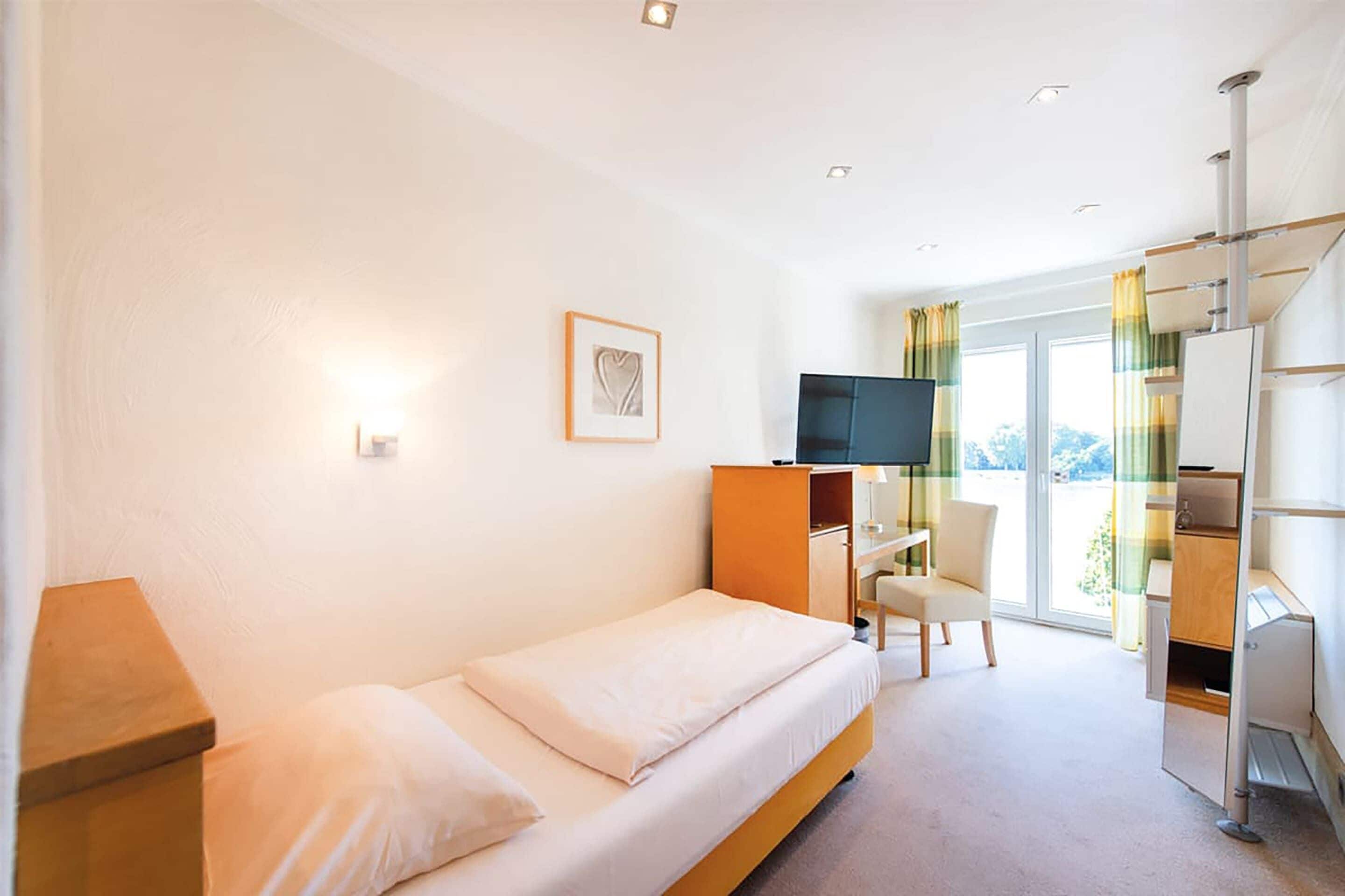 A hotel room with a bed, a desk, a chair, a TV, and a window with curtains.