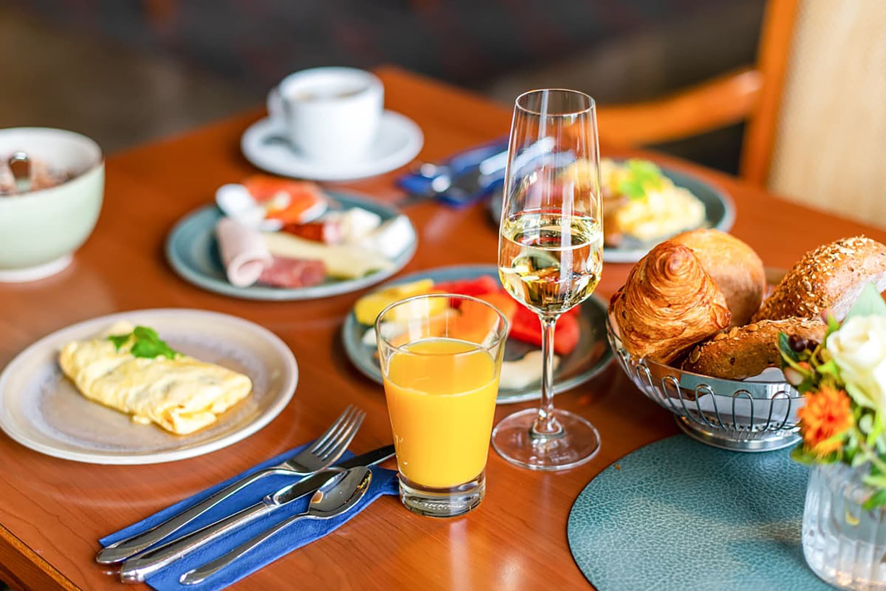A breakfast setting with plates of food, a glass of orange juice, and a glass of white wine on a wooden table.