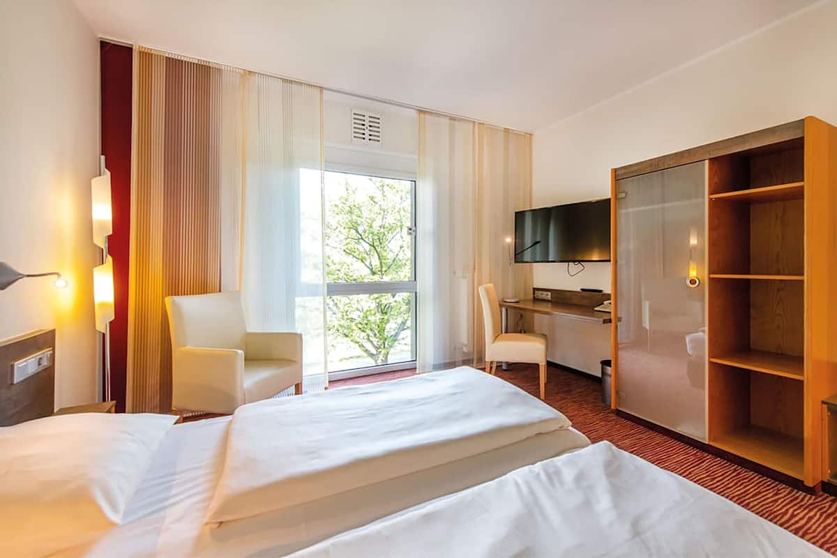 Una habitación de hotel con cama, escritorio, silla, televisor y armario.