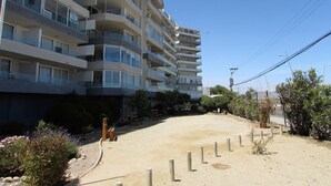 A multi-story building with balconies, a sandy ground area, and some vegetation. - 5.- HNA Mirador El Faro (La Serena)