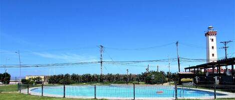 A swimming pool with a surrounding fence, a lighthouse in the background, and utility poles.