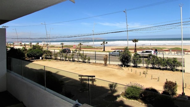 A balcony with a view of the beach, a road with cars, and a clear sky. - 5.- HNA Mirador El Faro (La Serena)