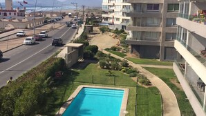 A residential area with a swimming pool, a road with cars, and a tall building with balconies. - 5.- HNA Mirador El Faro (La Serena)