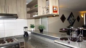 A modern kitchen with granite countertops, stainless steel appliances, wooden cabinets, and decorative items like wine glasses and a clock. - 5.- HNA Mirador El Faro (La Serena)