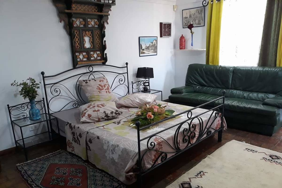 A bedroom with a bed, a nightstand, a green sofa, and a decorative wall piece.