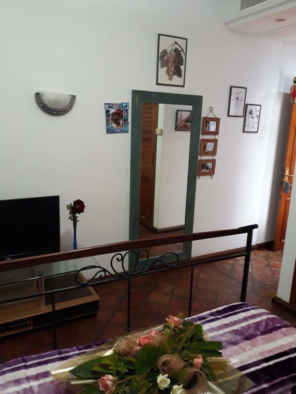 Una habitación con televisión, espejo y un arreglo floral sobre una mesa.