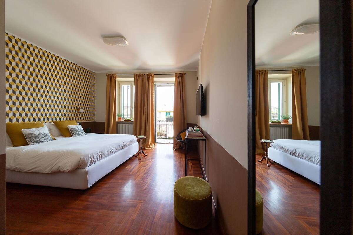 A hotel room with two beds, a desk, a chair, a mirror, and a patterned wall.