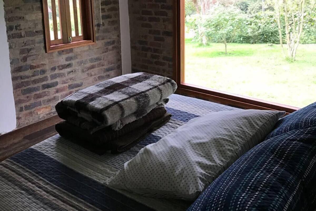 A bedroom with a large window, a wooden ceiling, and a brick wall.